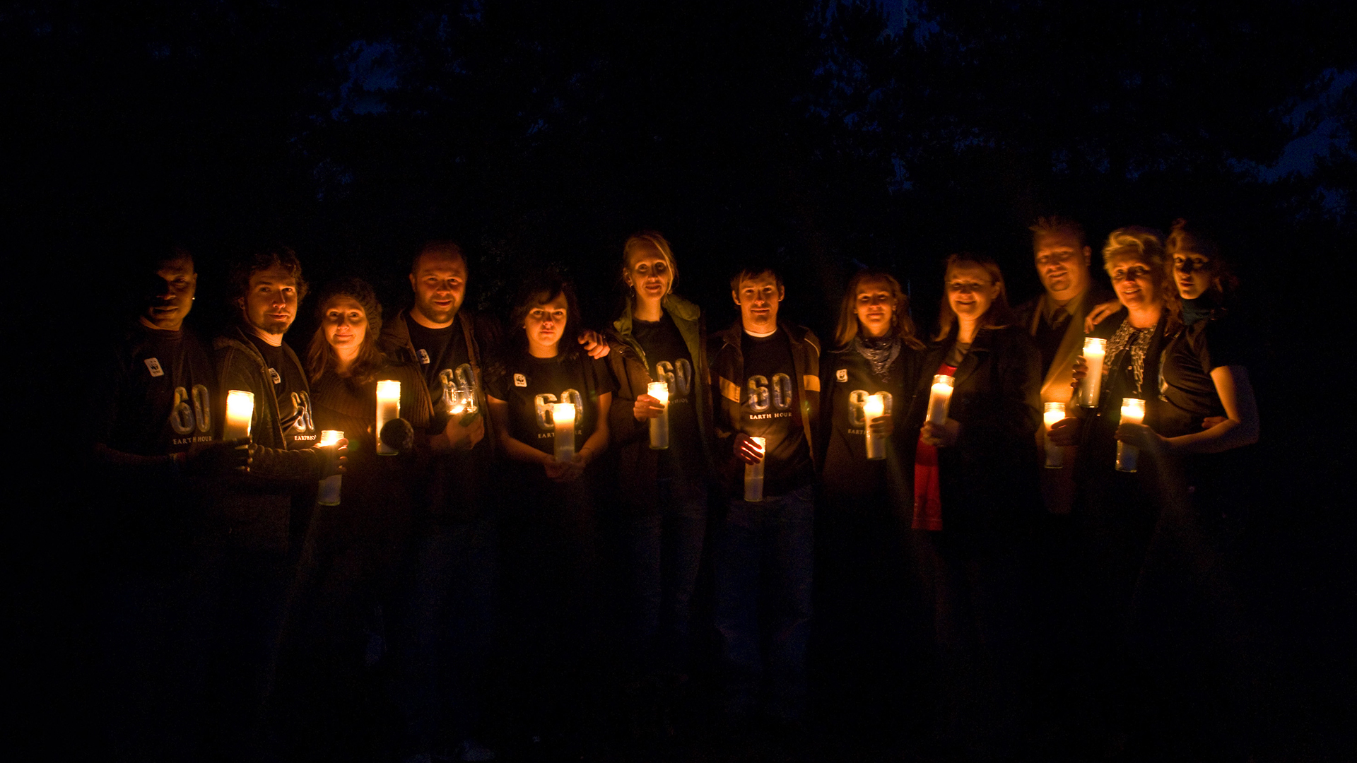 Students stand with candles in the dark to celebrate Earth Hour