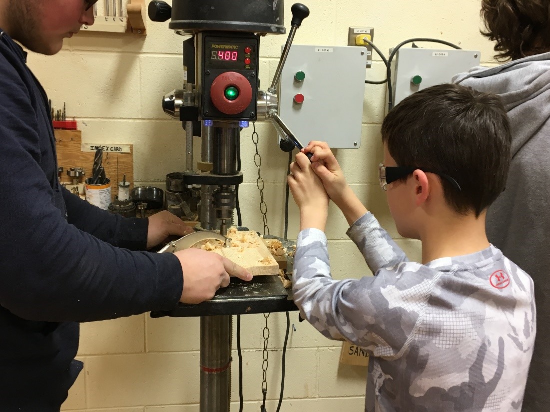 A high school student assists a young elementary school student in creating bird habitats in the wood shop